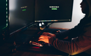 A person's hands are visible on a gaming keyboard, with a large monitor displaying data or code, indicating an intense focus on a digital task or project.