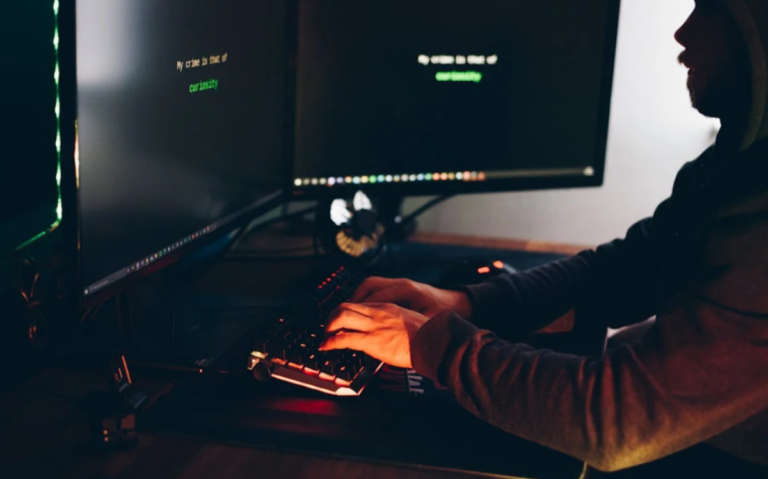 A person's hands are visible on a gaming keyboard, with a large monitor displaying data or code, indicating an intense focus on a digital task or project.