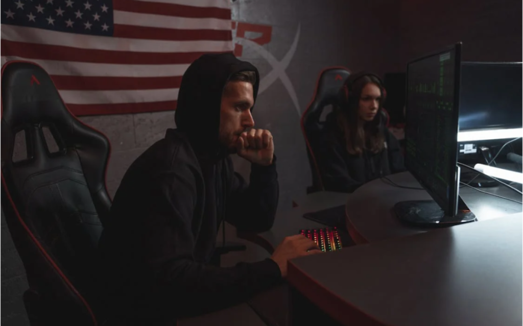 Two individuals in hooded attire intently focused on a computer screen, suggesting the exploration of digital systems or potential cybersecurity activities.