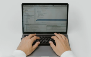 Hands typing on a laptop keyboard while a software development environment is displayed on the screen, suggesting the process of coding and programming.