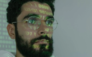 A person wearing glasses with a digital display projected onto their face, suggesting the use of advanced computer interfaces or augmented reality technology.