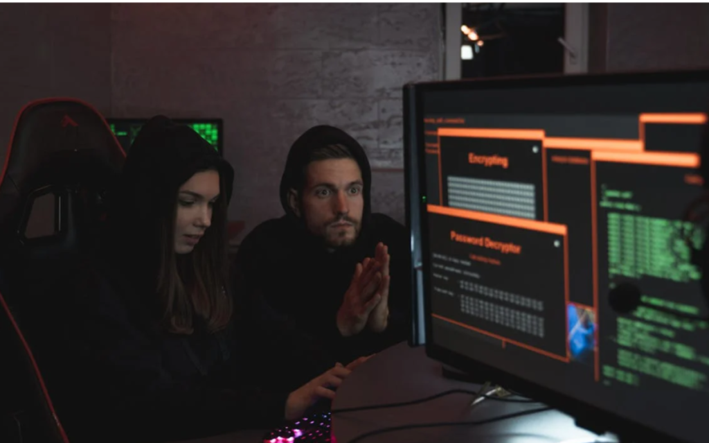 Two individuals intently focused on a computer screen displaying complex digital information, suggesting the collaborative nature of cybersecurity or hacking activities.