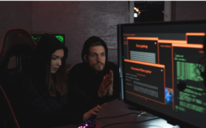 Two individuals intently focused on a computer screen displaying complex digital information, suggesting the collaborative nature of cybersecurity or hacking activities.