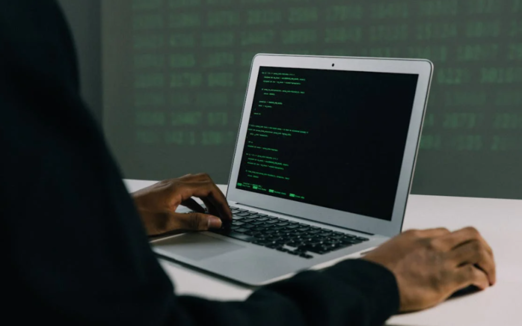 A person's hands typing on a laptop computer, the screen displaying lines of code, suggesting the activities involved in software development or programming.