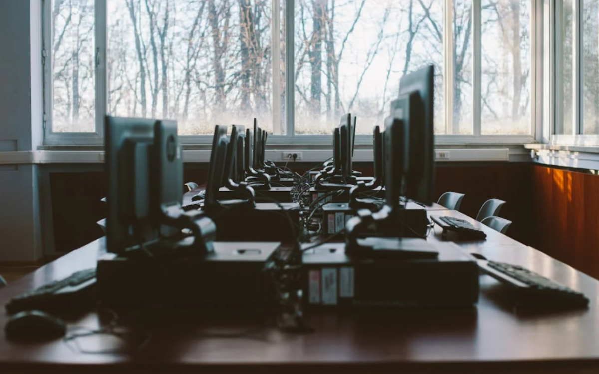 A dimly lit office space with rows of computer monitors and equipment, suggesting a workspace focused on technology or digital activities.