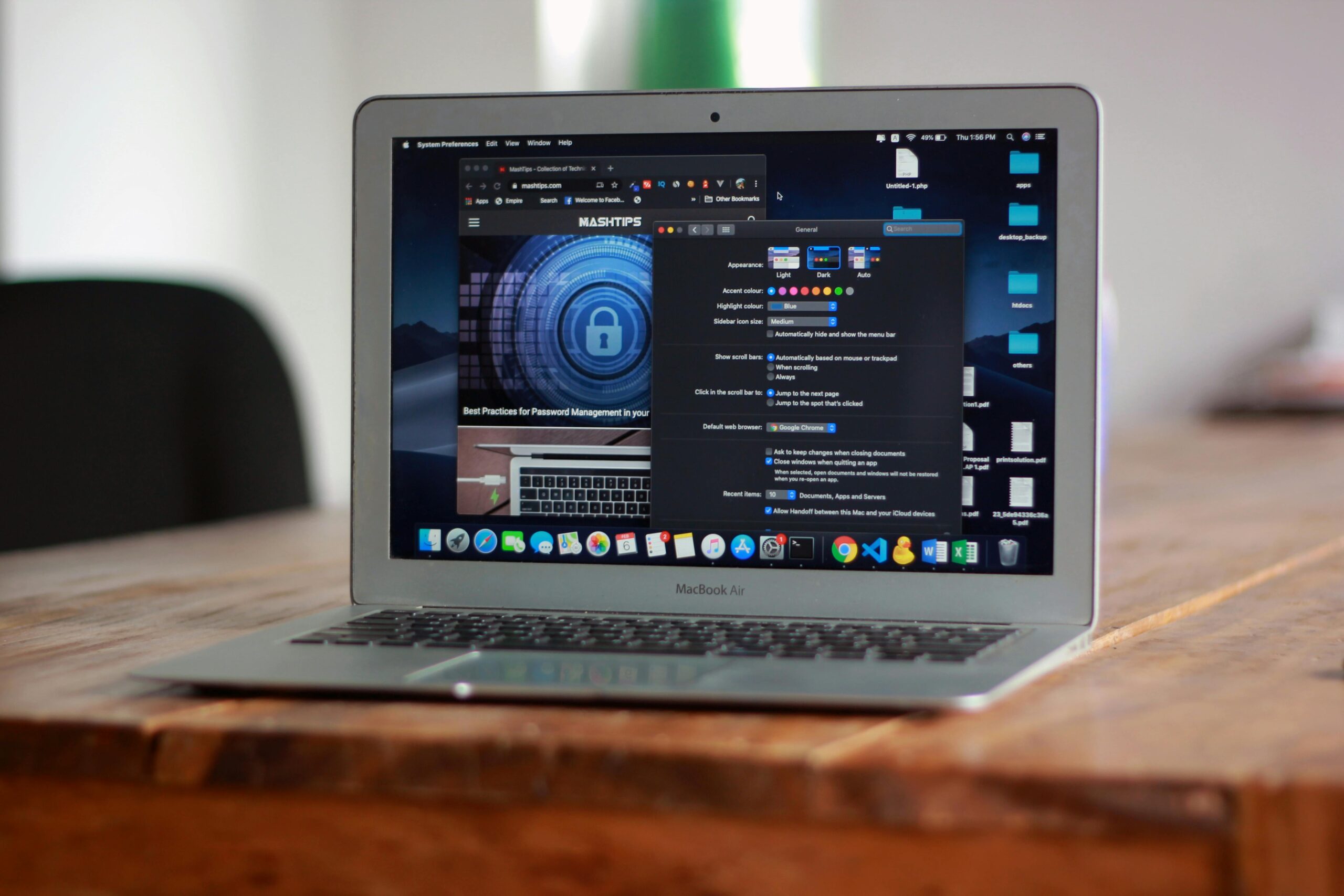 Laptop computer on a wooden desk, screen showing Mac system preferences and a cybersecurity webpage, with application icons in the dock
