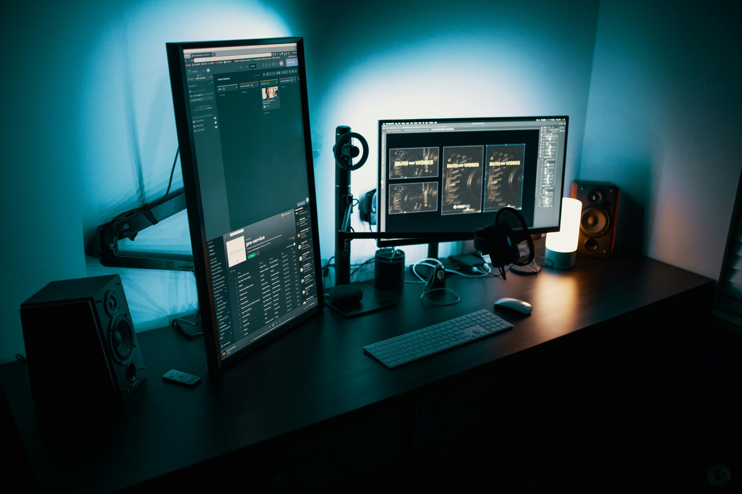 Professional dual-monitor workstation with blue ambient lighting, showing digital interface screens, keyboard, speakers, and computer accessories on a dark desk