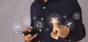 Digital interface showing 'Net Zero' concept with interconnected icons representing renewable energy, recycling, and sustainability, with a person touching the central 'Net Zero' button.