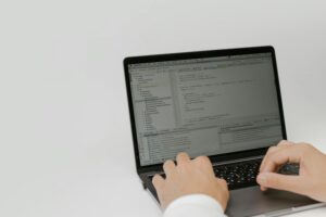 An image of a person's hands typing on a laptop computer, which displays code and development tools on the screen.