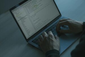 Close-up view of a person's hands working on a coding or software development task on a laptop computer.