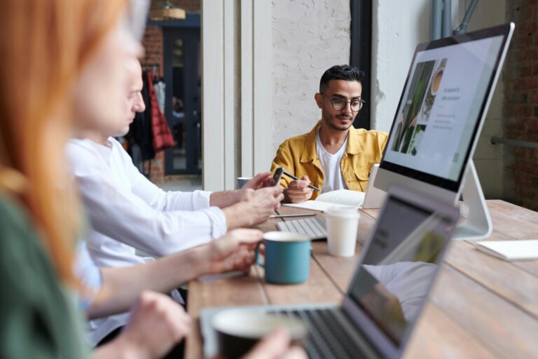 Two coworkers collaborating on a project in a modern, open office space with a computer screen and notes visible.