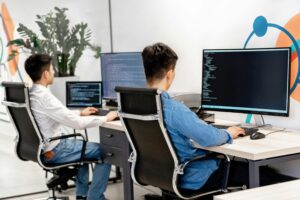 Two software developers or programmers working at desks, focused on their computer screens displaying code.