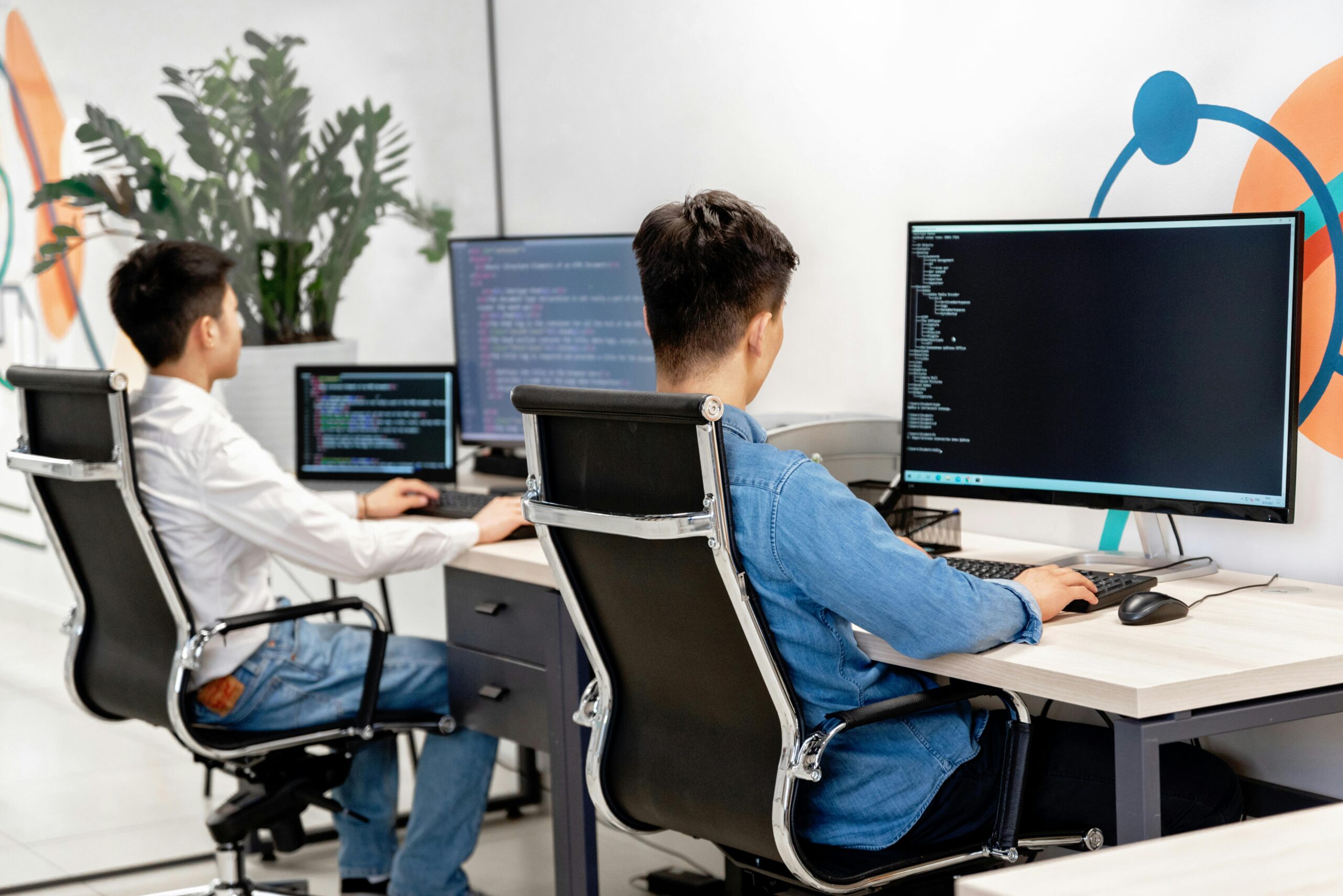 Two software developers or programmers working at desks, focused on their computer screens displaying code.