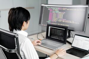 An individual focusing intently on the laptop and computer screens in front of them, engaged in software development or coding work.