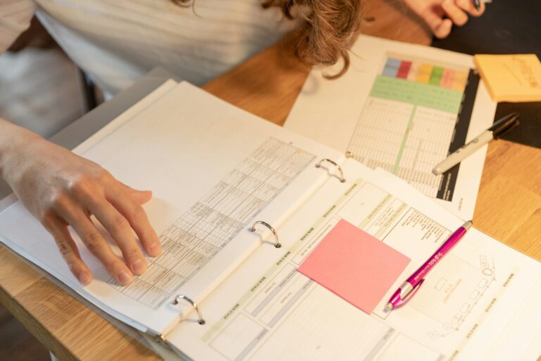 Detailed Data Organization: The desk surface is covered with various paperwork, forms, and a binder, indicating a focused effort to meticulously organize and manage detailed information.