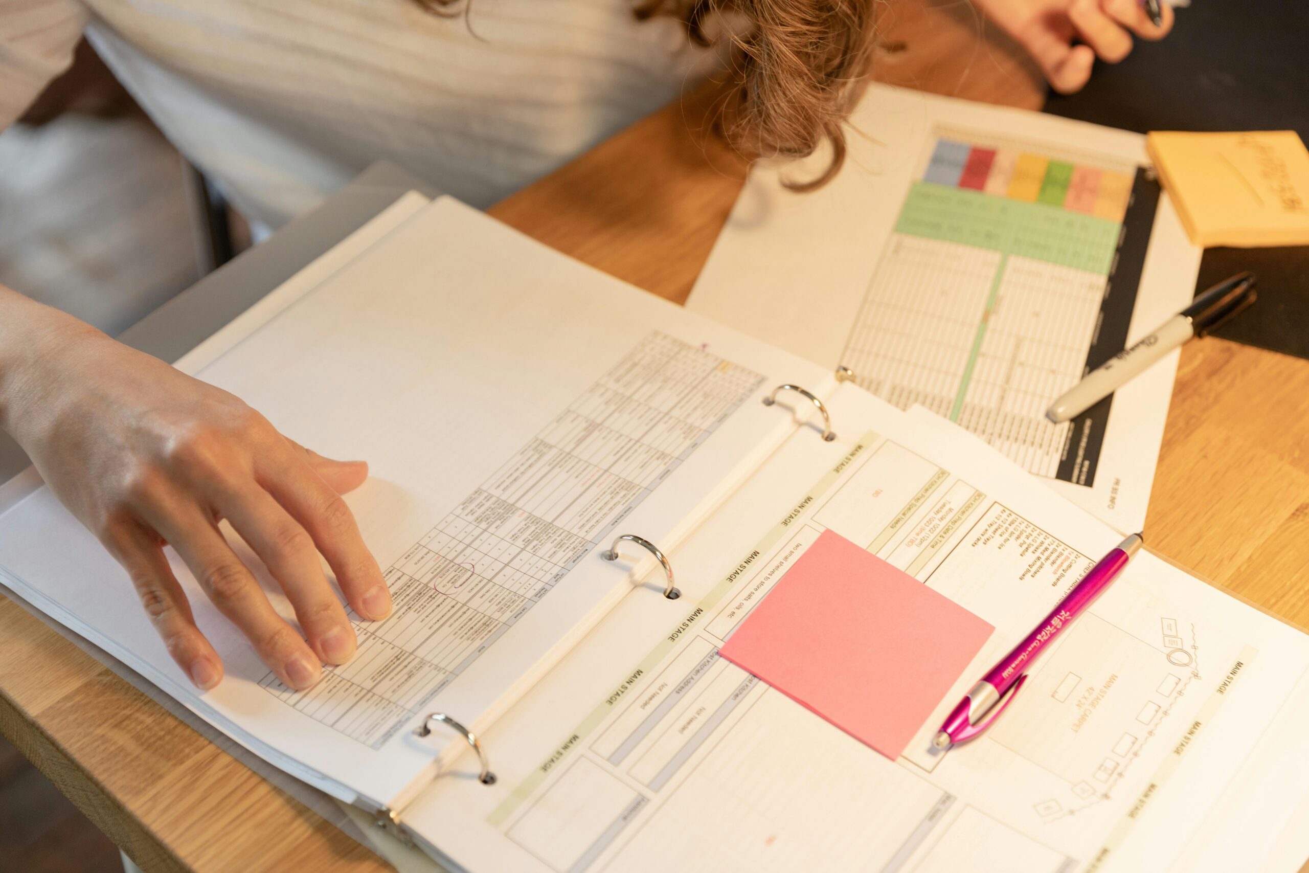 Detailed Data Organization: The desk surface is covered with various paperwork, forms, and a binder, indicating a focused effort to meticulously organize and manage detailed information.