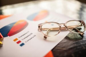 Detailed company information and financial data displayed on documents, accompanied by a pair of eyeglasses, implying a focus on analysis and decision-making.
