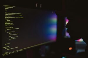 Coding workspace with a computer screen showcasing lines of code amidst a colorful, shadowy environment.