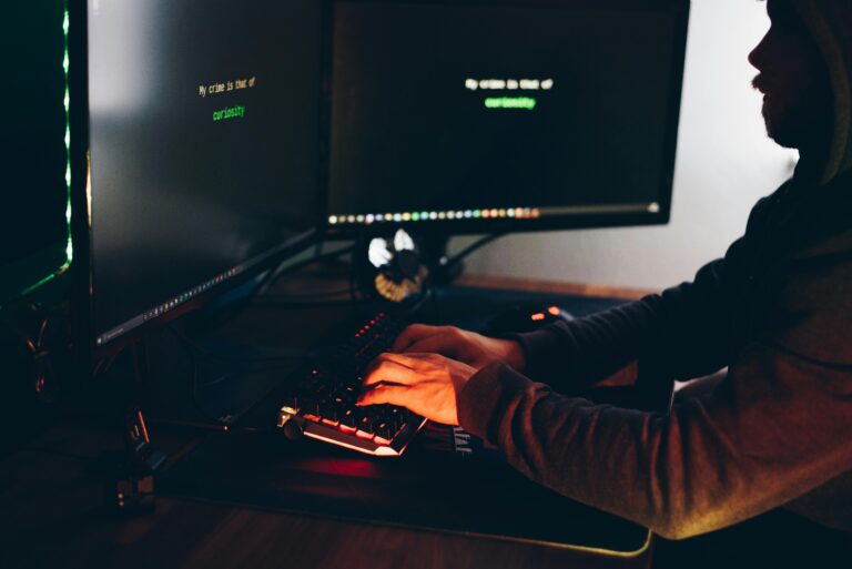 A close-up view of a person's hands typing on a keyboard, with a computer screen visible in the background showing a line of text that suggests a fascination with the digital world.
