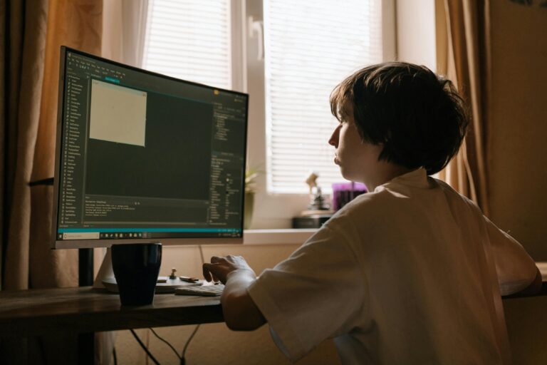 A young boy intently focusing on a computer screen, which appears to display code or programming software, suggesting he is engaged in coding or software development.