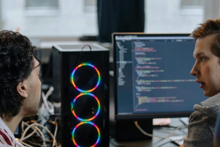 Two programmers intensely focused on the code displayed on their computer screens while working together.