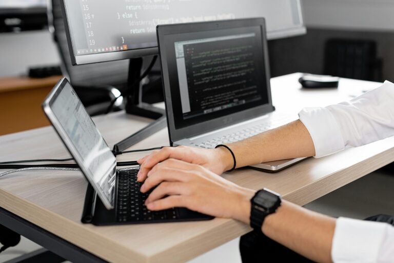 Workspace of a computer programmer or software engineer, featuring multiple devices and screens displaying code and programming environments.