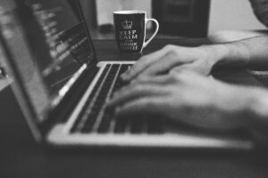 A monochrome image showing hands working on a laptop, with a coffee mug prominently displayed.