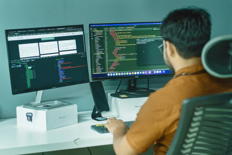 Immersed in programming, a developer diligently examines lines of code on multiple displays while working at their desk.