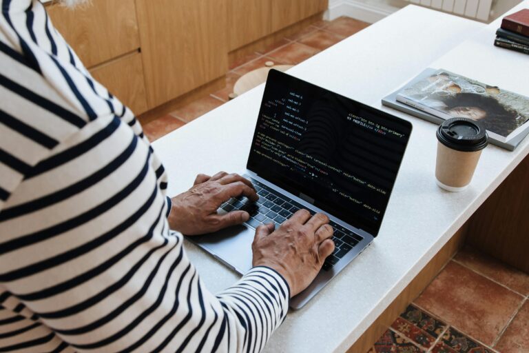 Close-up view of a person's hands working on a laptop, the screen showing programming text.