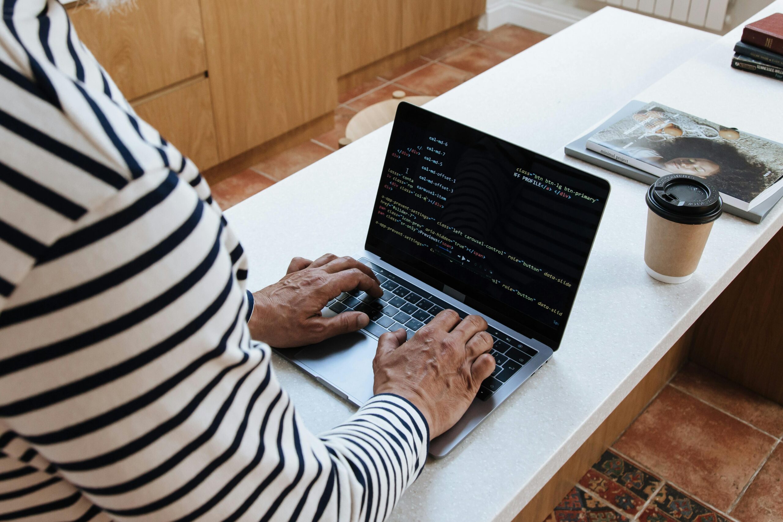 Close-up view of a person's hands working on a laptop, the screen showing programming text.