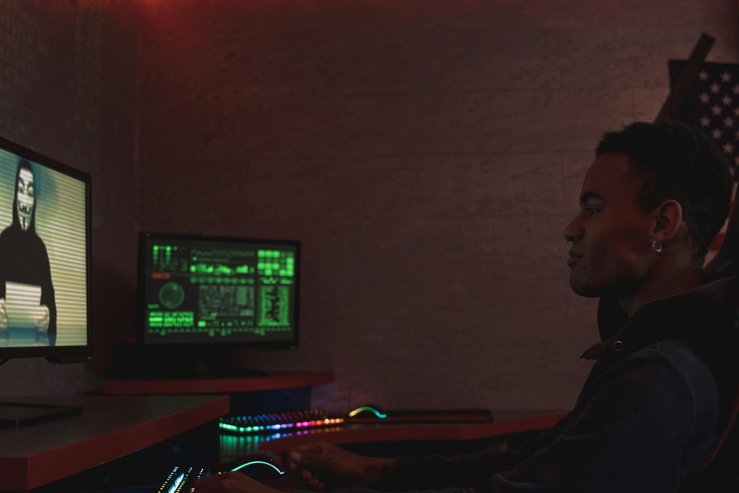 The profile of a person sitting at a desk, their face obscured as they interact with a computer displaying intricate digital information.