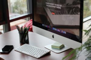 Productive workspace with an Apple display showcasing a web page about free Bootstrap themes, complemented by office accessories and a touch of greenery on the desk.