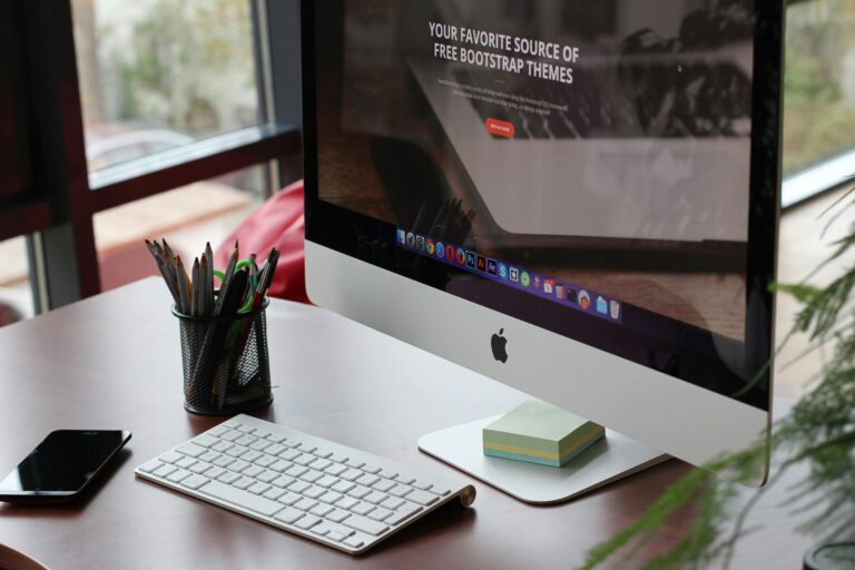 Productive workspace with an Apple display showcasing a web page about free Bootstrap themes, complemented by office accessories and a touch of greenery on the desk.