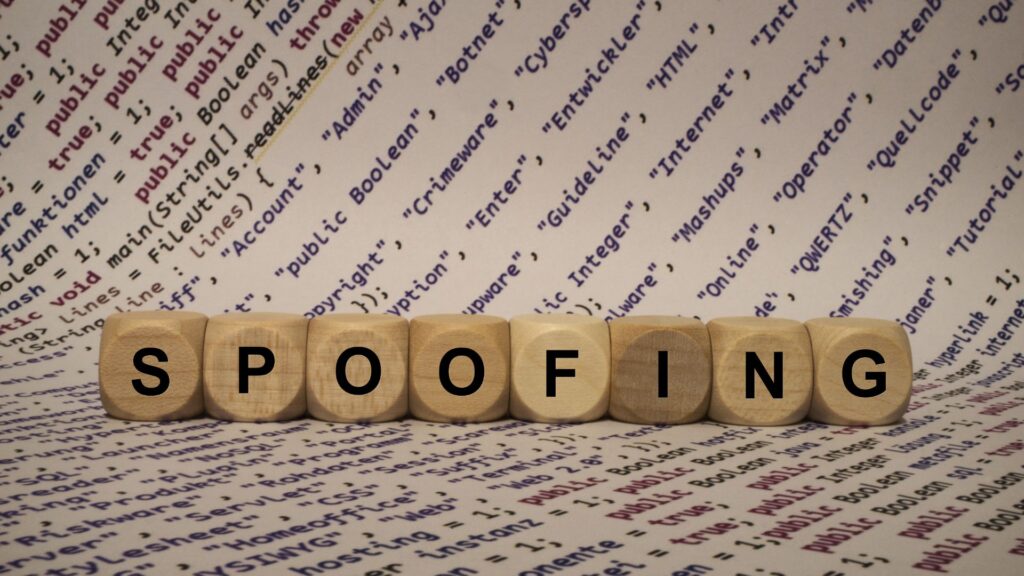 The word "SPOOFING" spelled out using wooden letter tiles on a background of text, suggesting the deceptive nature of spoofing attacks and the importance of being vigilant against such threats in digital communications.
