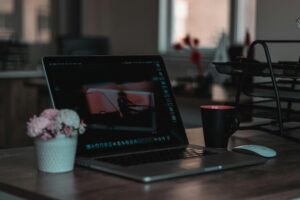 A focused view of a laptop computer screen, showcasing a photo editing or creative software interface, surrounded by a minimalist desk setup with floral and mug accents.
