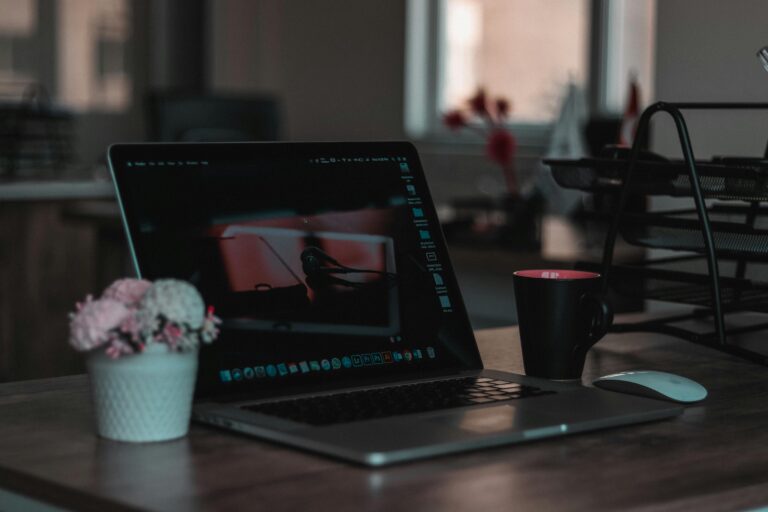 A focused view of a laptop computer screen, showcasing a photo editing or creative software interface, surrounded by a minimalist desk setup with floral and mug accents.