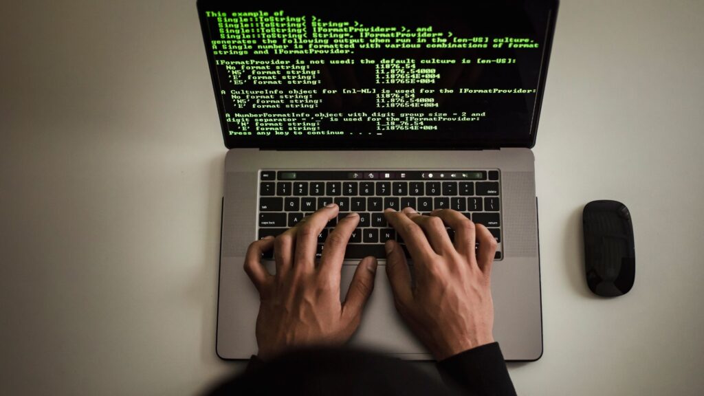The image depicts a person typing on a laptop, with a programming code displayed on the screen, suggesting a technical or coding-related context.