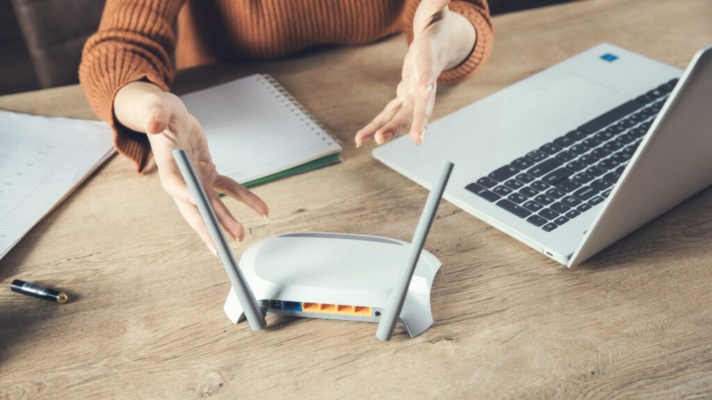 A person's hands interacting with a laptop and wireless router, suggesting the use of technology and connectivity.